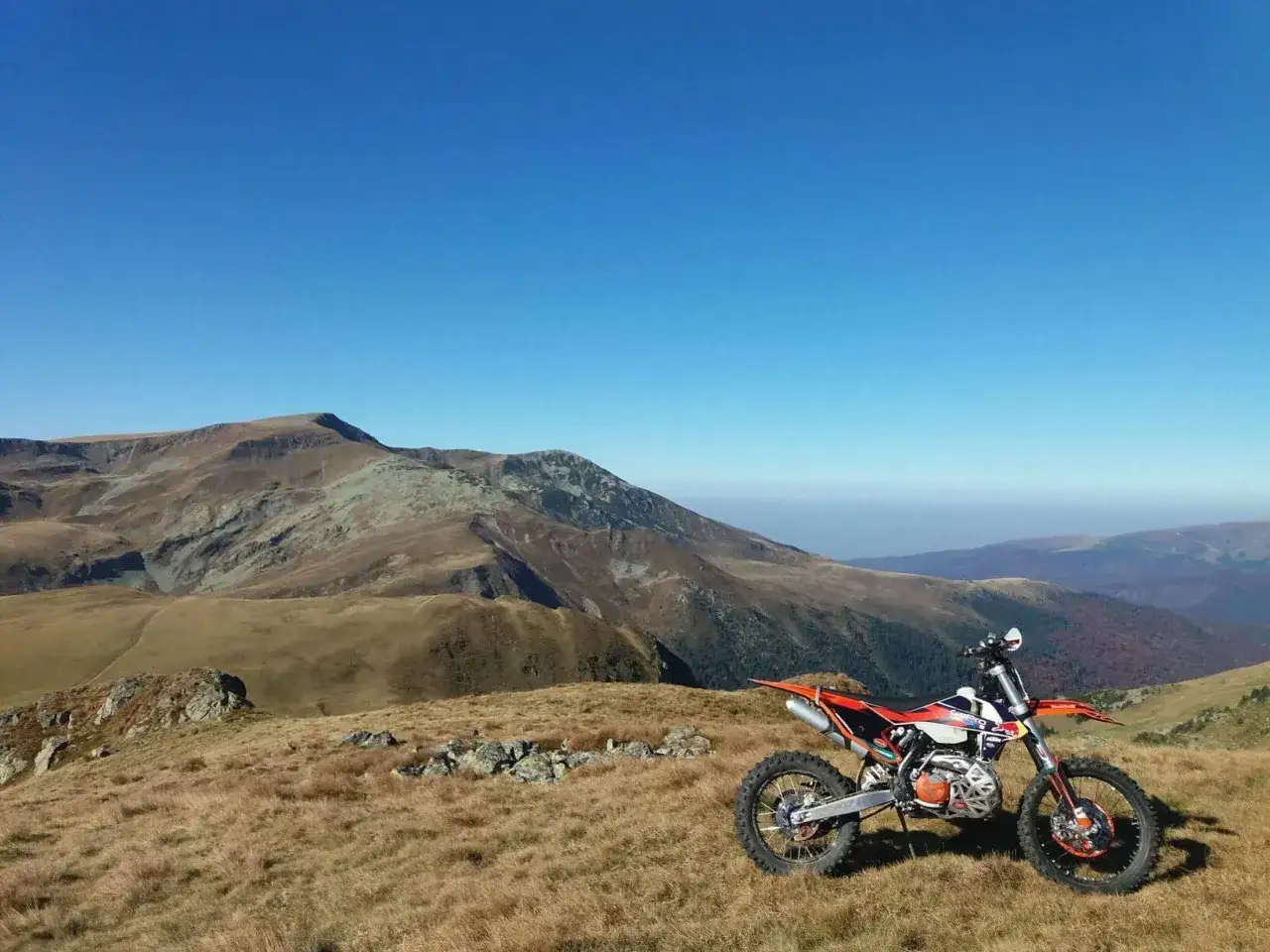 Pomarańczowy motocykl terenowy na tle g&oacute;rskiej panoramy. Idealne miejsce na **trasę motocyklową w Rumunii**.