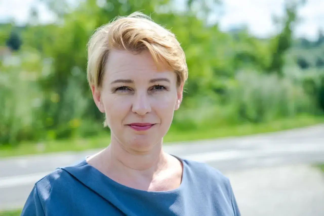 Katarzyna Kierzek Koperska z uśmiechem patrzy w obiektyw na tle zieleni.