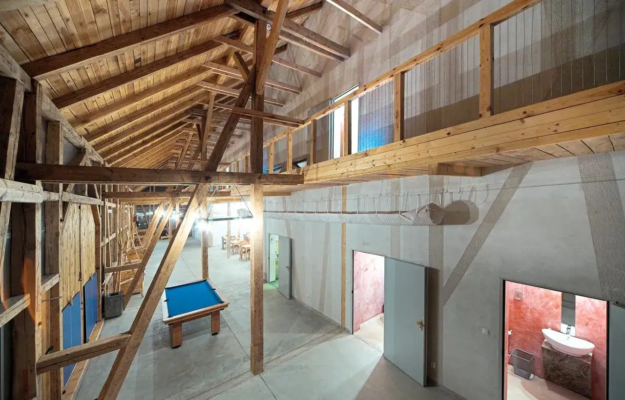 Przekształcenie budynku gospodarczego na mieszkalny. Wnętrze z drewnianymi belkami, stołem bilardowym i widokiem na łazienkę.