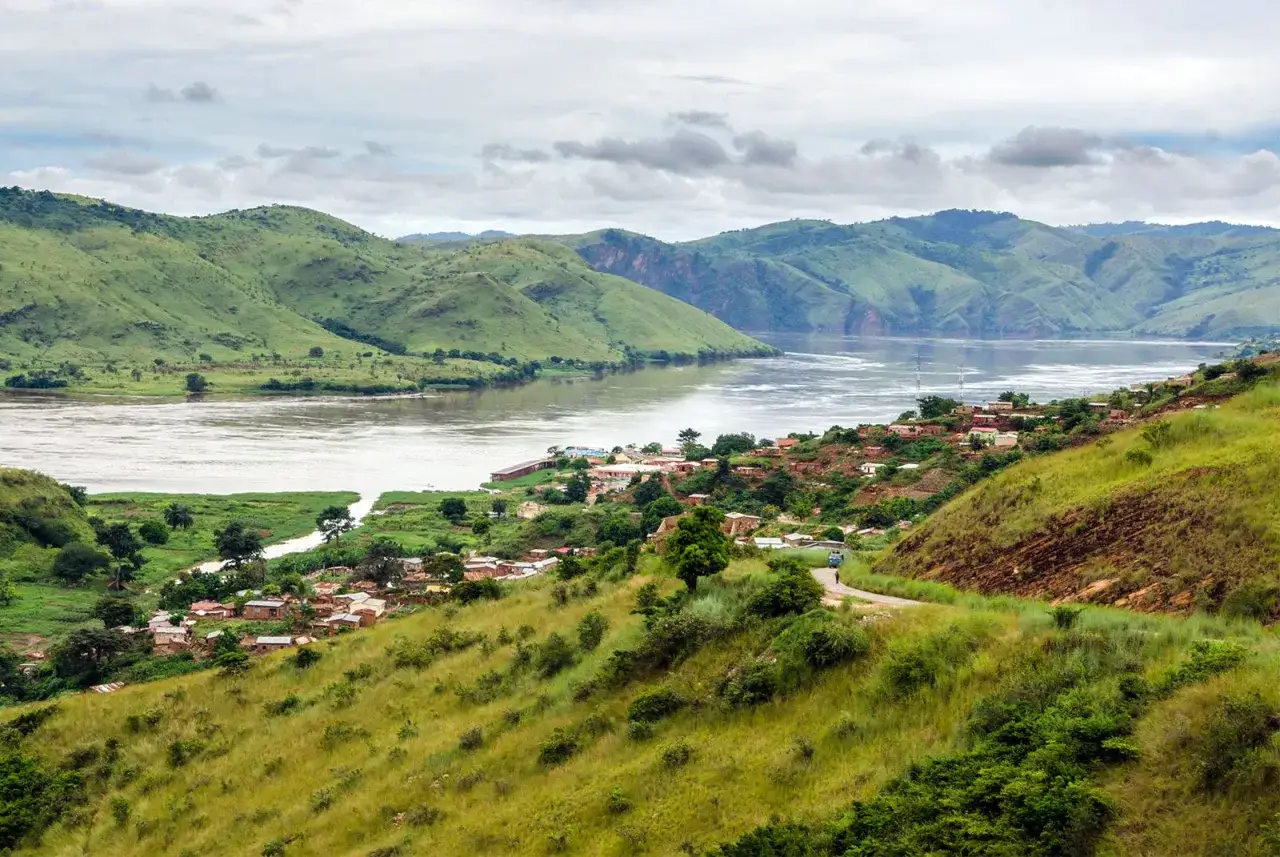 Zielona dolina z rzekami w Afryce, z wioską na zboczu wzg&oacute;rza i g&oacute;rami w tle.