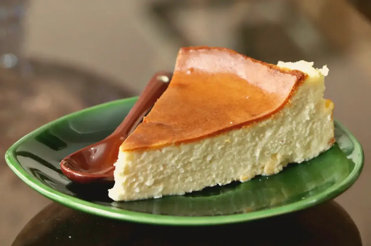 Pyszny sernik wiedeński na zielonym talerzyku, z brązową łyżeczką. Idealny, gdy zastanawiasz się, jak zrobić sernik wiedeński.