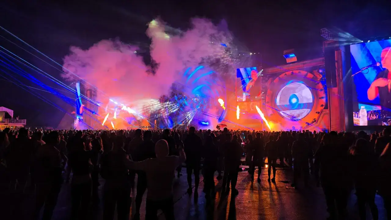 Tłumy bawią się na festiwalu Sunrise Festival 2026. Scena rozświetlona laserami, dymem i płomieniami, a na ekranach DJ.