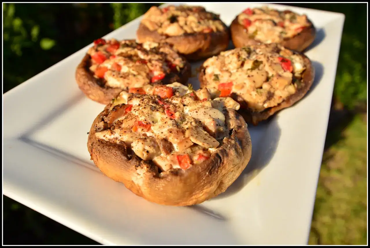 Pięć pieczarek faszerowanych na grilla, z papryką i serem, na białym talerzu.