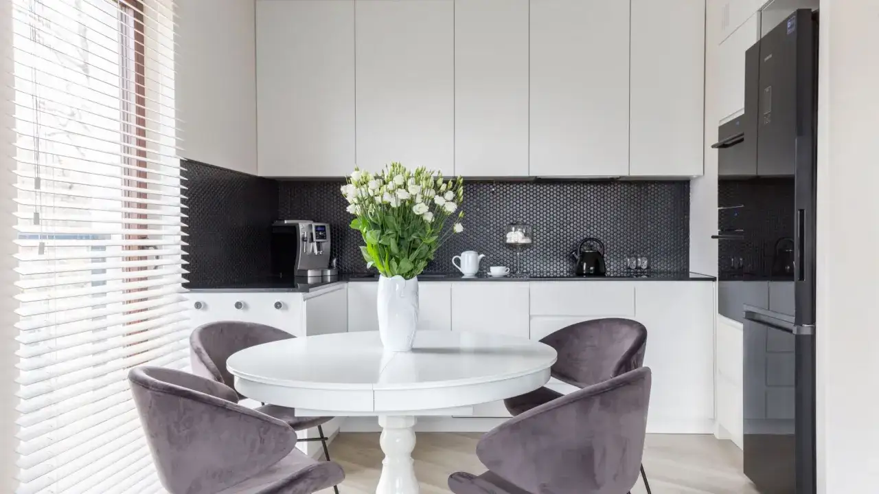 Stylowa, mała kuchnia w stylu nowojorskim z białymi szafkami, czarnym mozaikowym backsplash i okrągłym stołem z aksamitnymi krzesłami.