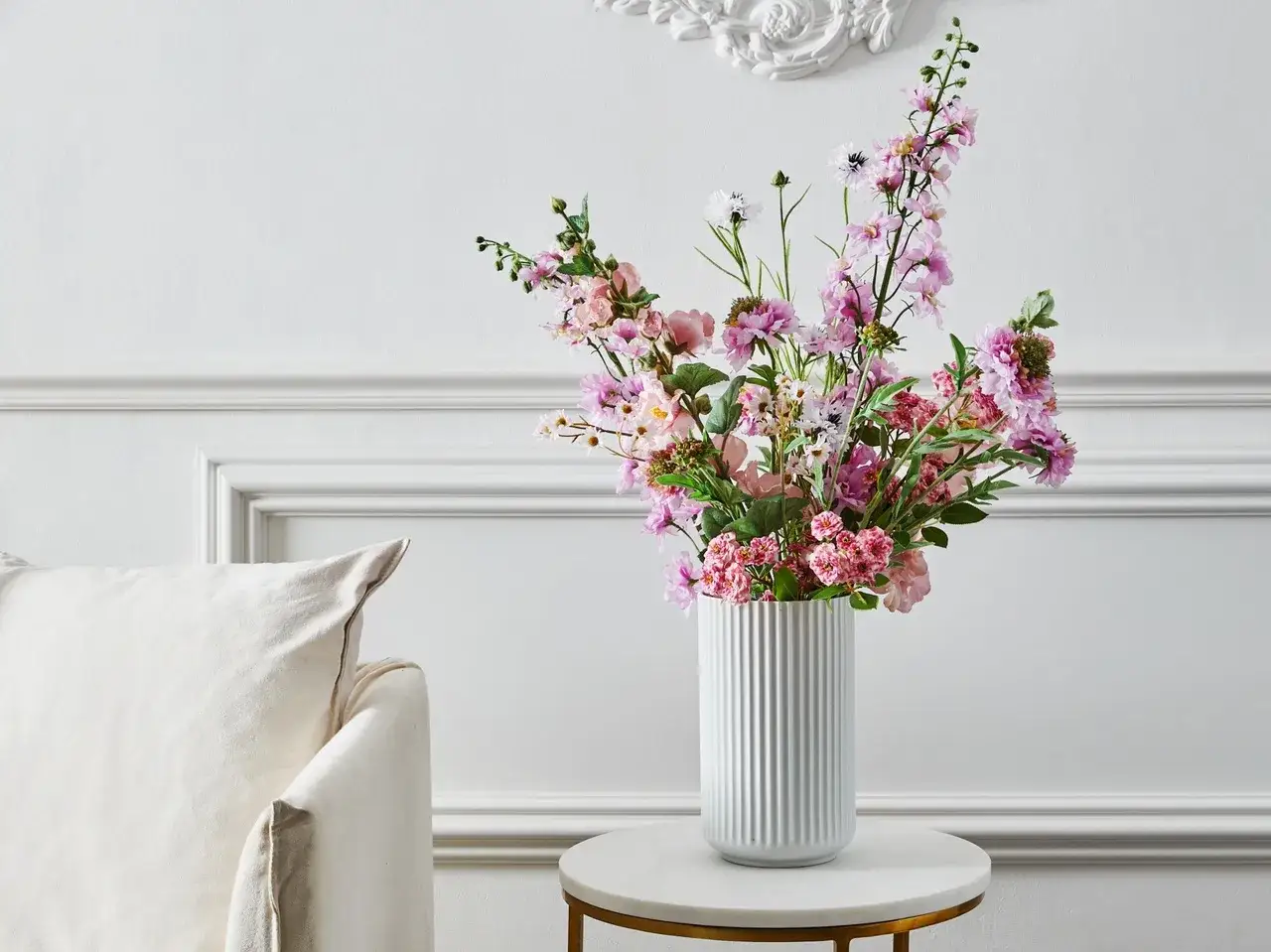 Piękny bukiet kwiatów bukietowych w wazonie, otoczony jasną kanapą i elegancką ścianą.