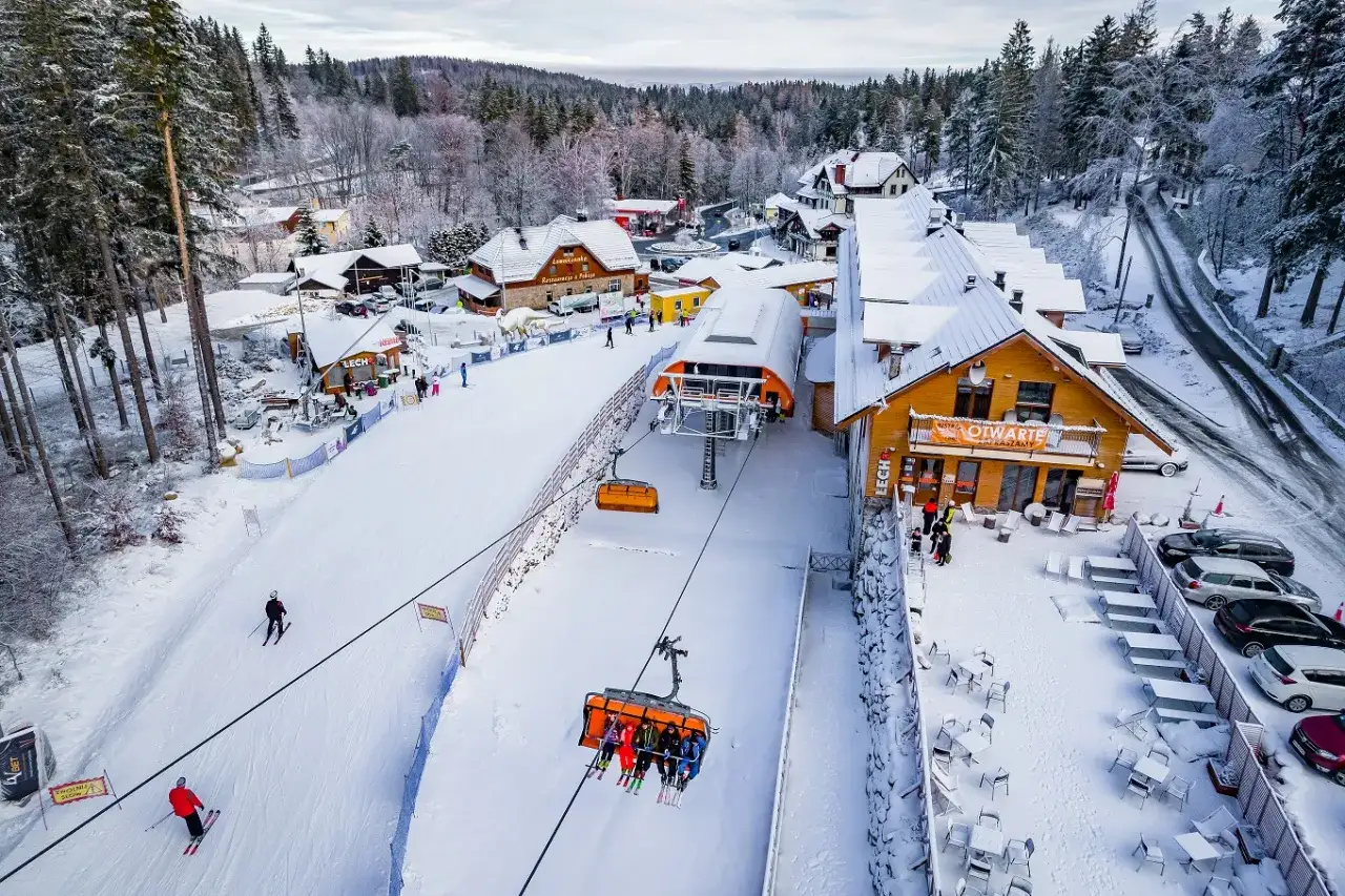 Zimowy dzień na stoku. Wyciąg narciarski Karpacz z gondolami w powietrzu, narciarze na śniegu i przytulne górskie budynki.