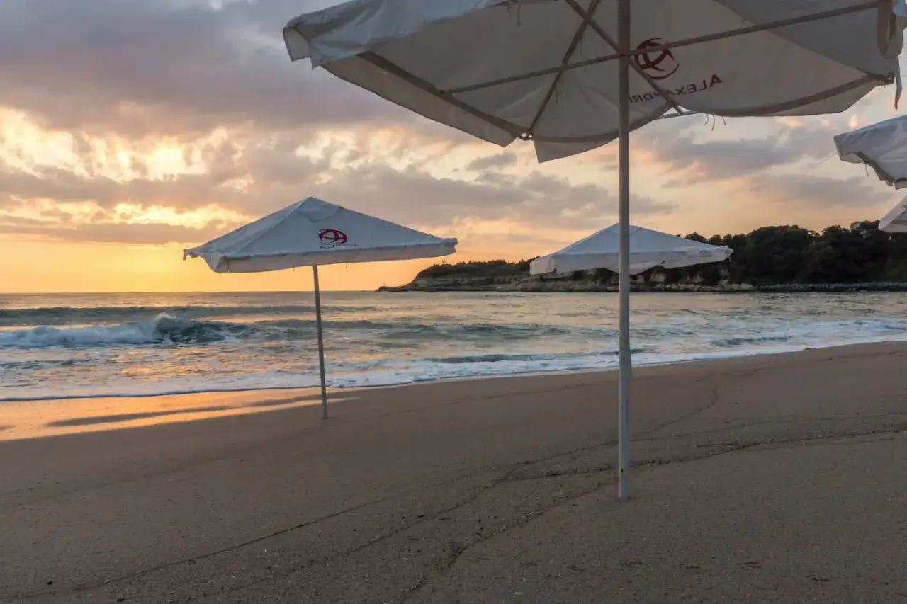 Piękny zach&oacute;d słońca nad morzem, plaża z parasolami zaprasza na relaks. To idealne miejsce na wakacyjne carewo atrakcje.