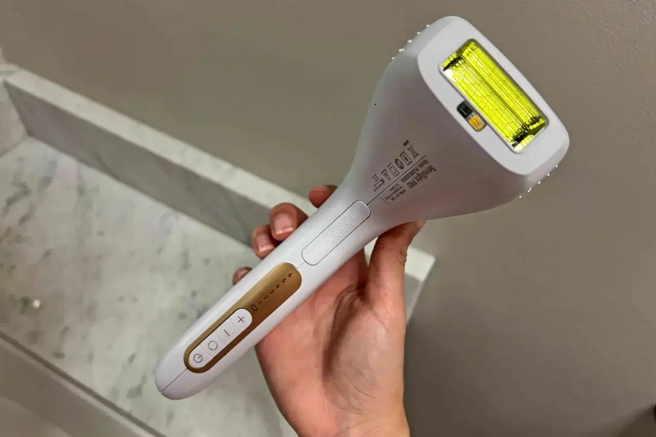 Biały depilator laserowy trzymany w dłoni, z widocznym panelem sterowania i lampą. Pokazuje, jak działa depilator laserowy, emitując światło.