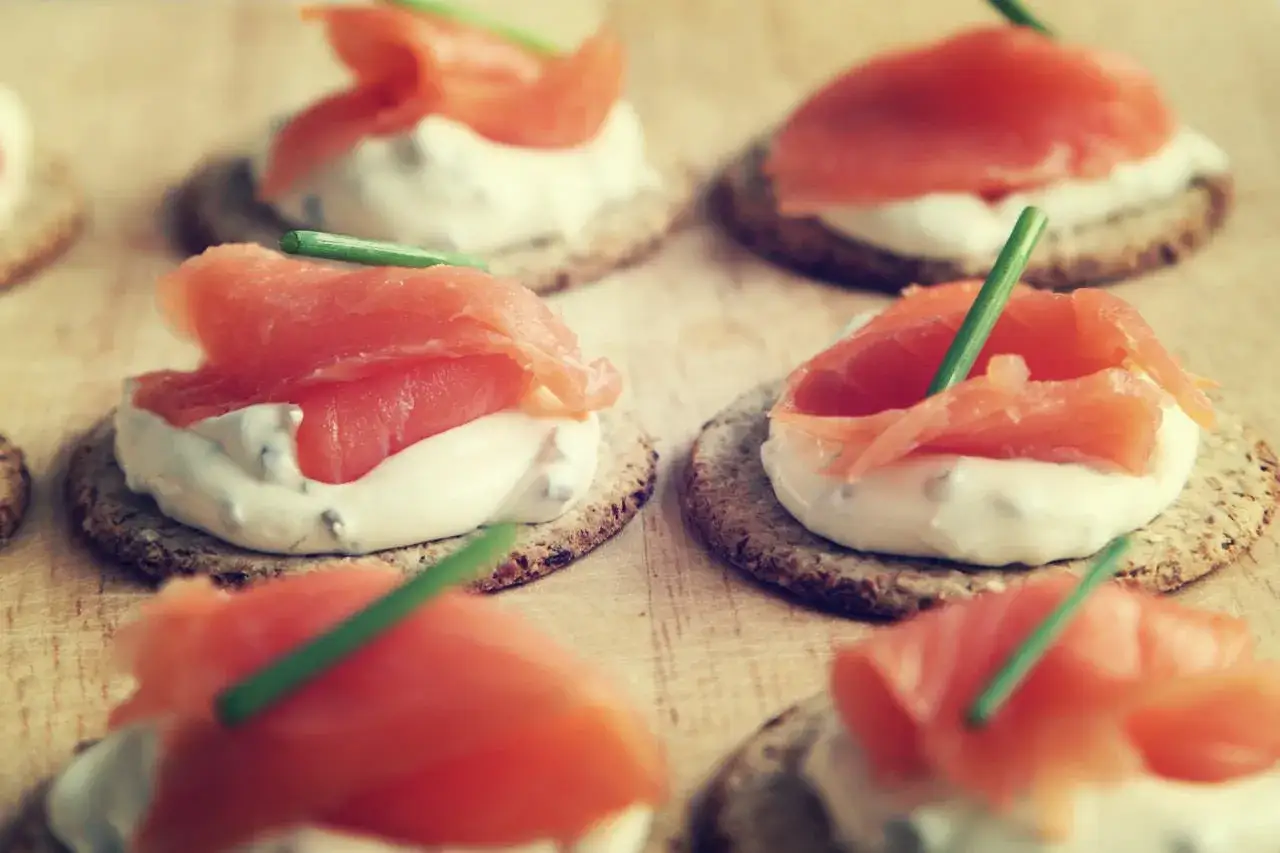 Wykwintne przystawki finger food: krakersy z kremowym serkiem, łososiem i szczypiorkiem. Idealne na przyjęcie.