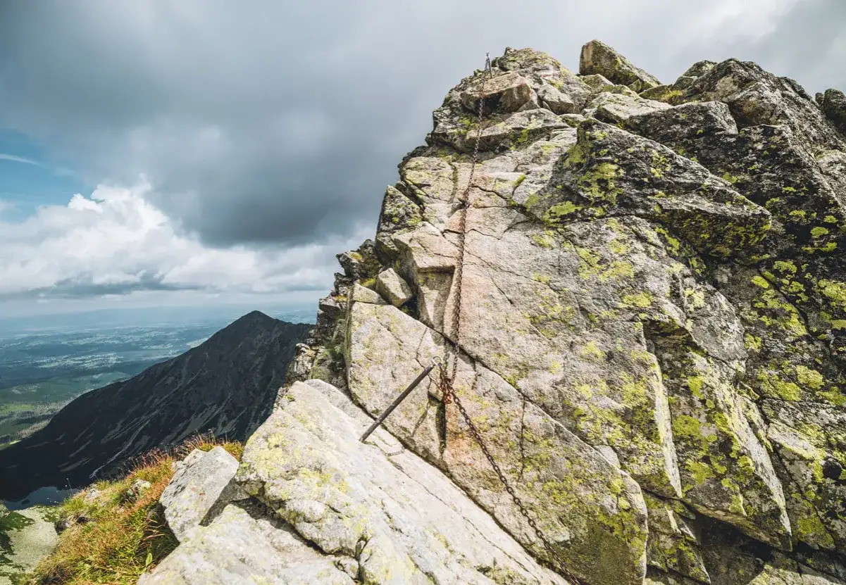 Kamienista grań, łańcuchy wspinaczkowe na zboczu, widok na dolinę i szczyt Mały Kozi Wierch.