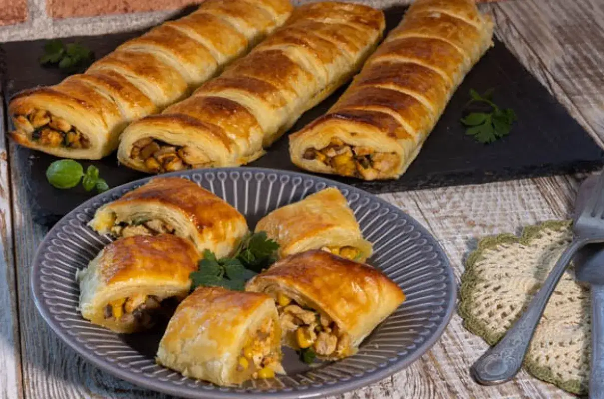 Złociste rolady z kurczakiem w cieście francuskim, podane na talerzu i desce. Pyszny kurczak w cieście francuskim kusi apetycznym wyglądem.