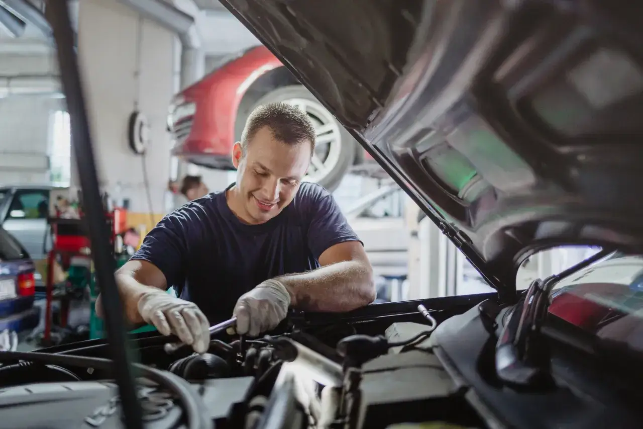 Mechanik w rękawiczkach naprawia silnik. To dobry przykład, jak otworzyć warsztat samochodowy, gdy pasjonuje Cię motoryzacja.