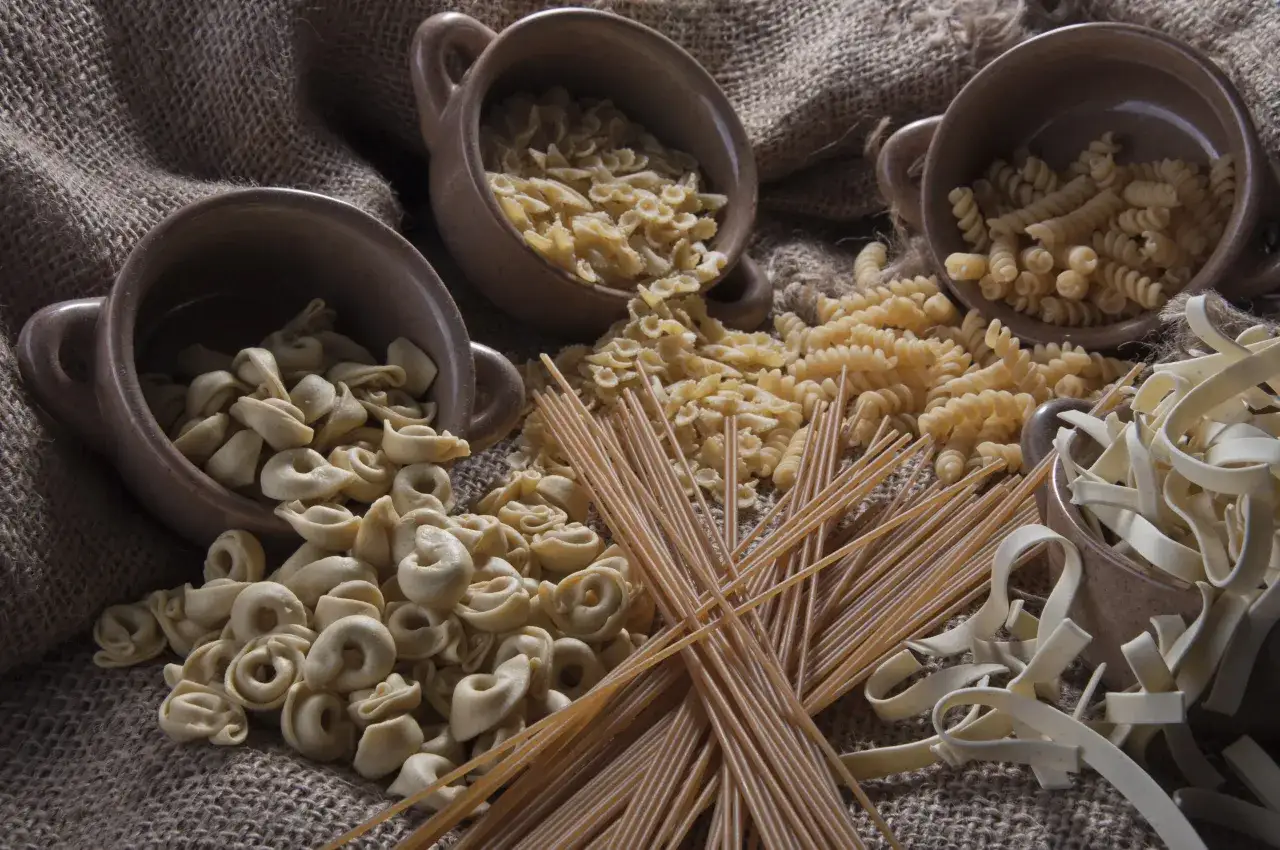 Kluski vs makaron: tortellini, farfalle, fusilli, spaghetti i tagliatelle w glinianych naczyniach na płótnie.