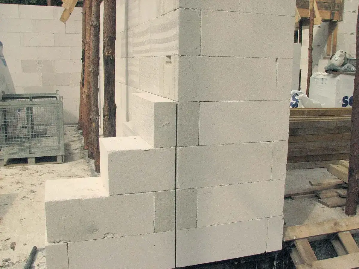 Budowa domu: kotwienie ścian działowych z bloczków betonowych. Widać elementy konstrukcyjne i materiały budowlane.