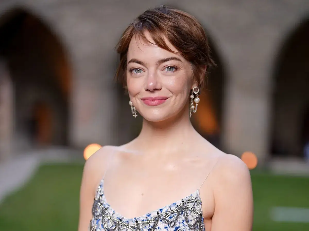 Emma Stone w krótkich, lekko potarganych włosach, które tworzą fryzury wyszczuplające twarz okrągłą. Delikatny makijaż i eleganckie kolczyki.