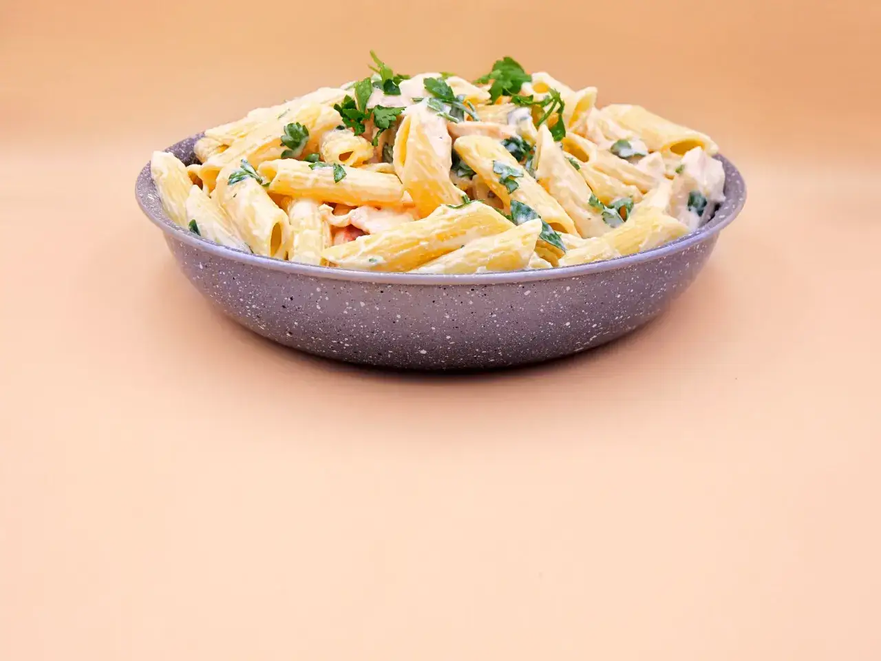 Pyszna carbonara z kurczakiem w kremowym sosie, posypana świeżą natką pietruszki, podana w szarej misce.