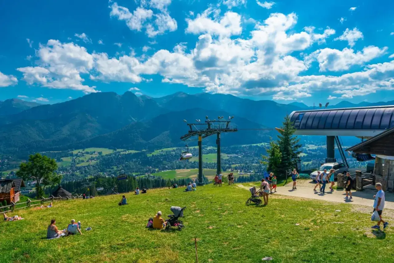Widok na góry z butorowy wierch kościelisko. Ludzie odpoczywają na zielonej trawie, w tle kolejka linowa i Tatry.