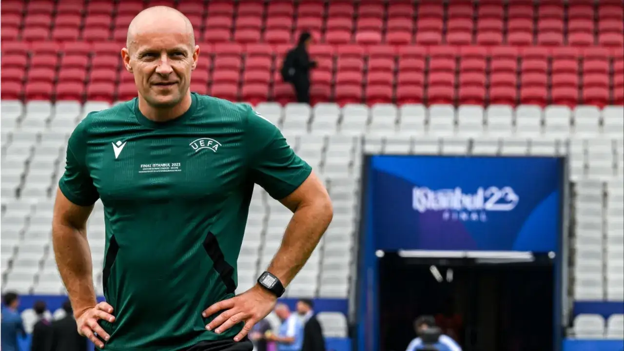 Sędzia piłkarski w zielonej koszulce UEFA na tle trybun stadionu. Zastanawiasz się, ile zarabia sędzia piłkarski w Lidze Mistrzów?