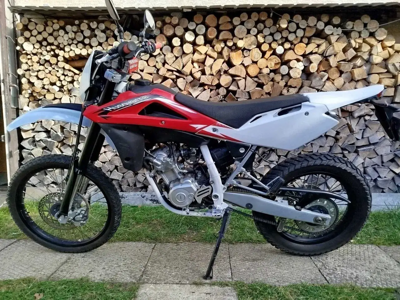 Czerwono-biały motocykl Husqvarna WR 125 na tle stosu drewna. Gotowy na przygodę!