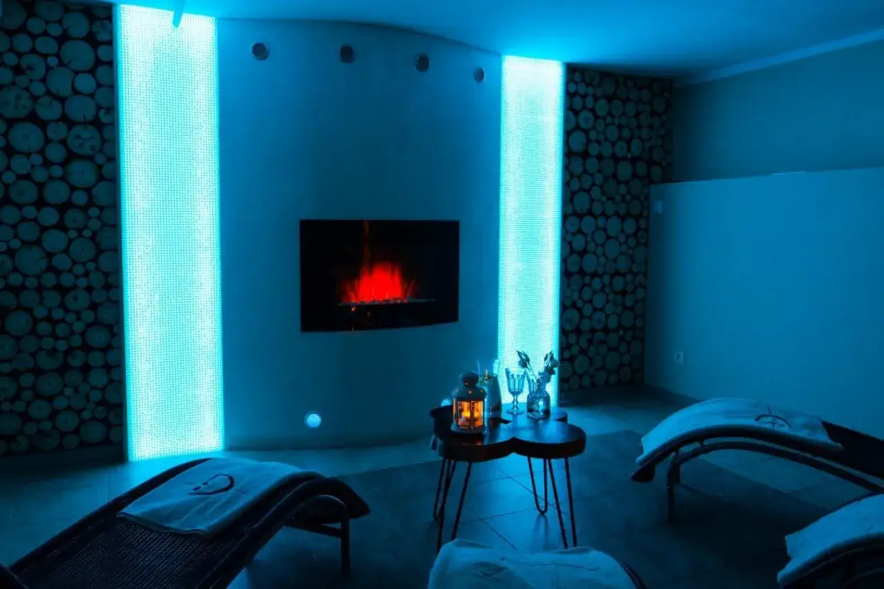 Relaks w nowoczesnym spa pod Poznaniem. Dwa leżaki, kominek z czerwonym ogniem i niebieskie podświetlenie tworzą przytulną atmosferę.