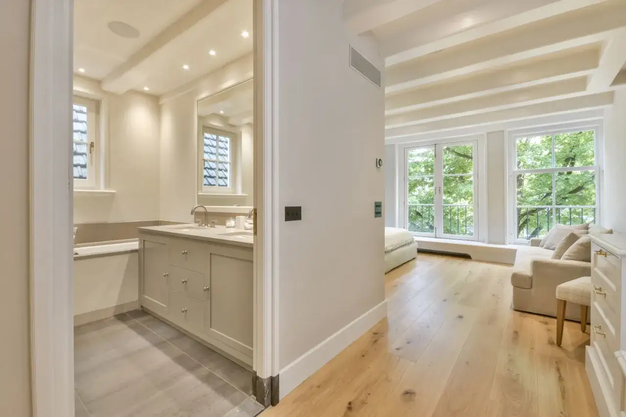 Łazienka z szarymi płytkami i sypialnia z drewnianą podłogą. Szare płytki to świetny wybór, jeśli zastanawiasz się, jakie płytki pasują do drewnianej podłogi.