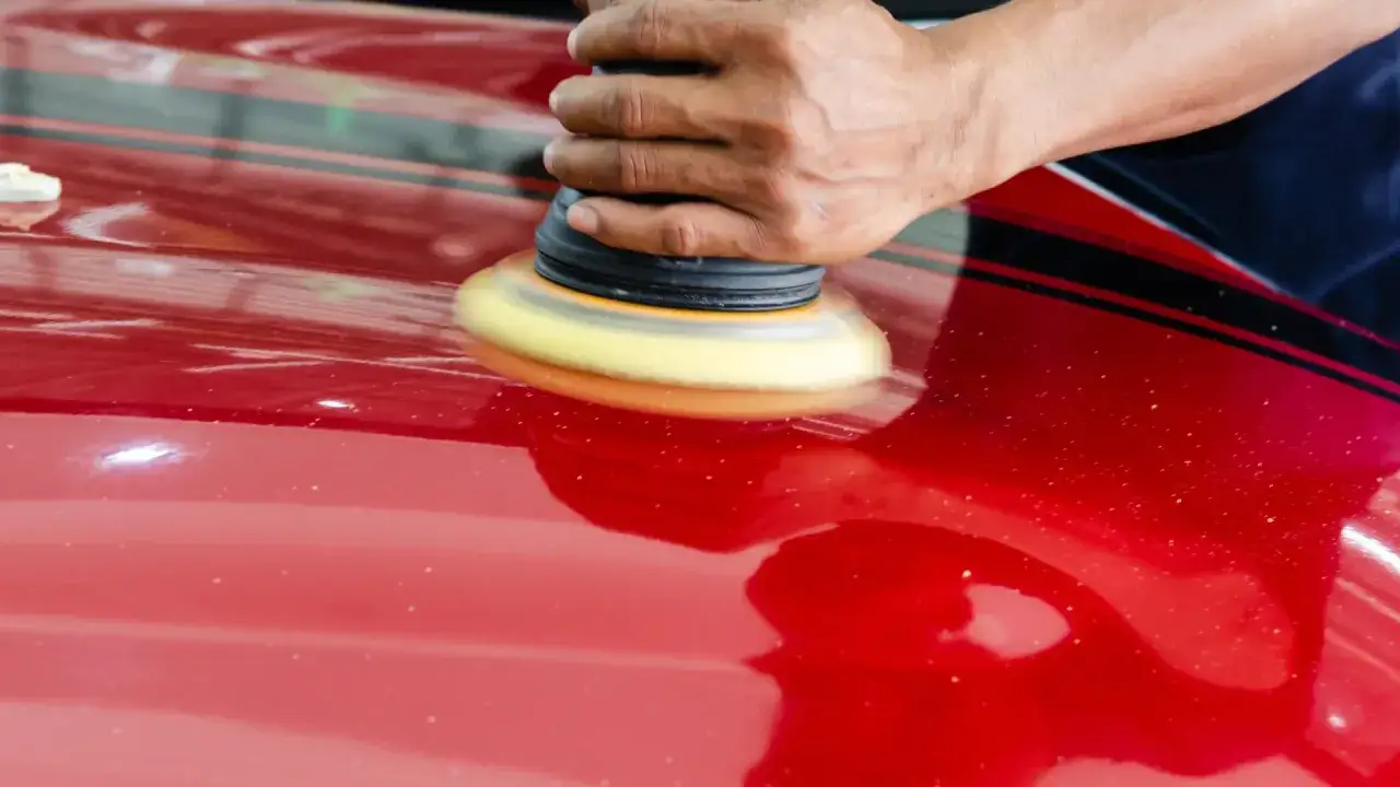 Dłoń poleruje czerwony lakier samochodu maszyną, pokazując, jak usunąć rysy i przywrócić blask.