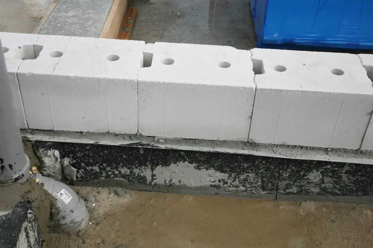 Białe bloczki na fundament, z otworami, ułożone na warstwie izolacji. To dobre bloczki na fundament.