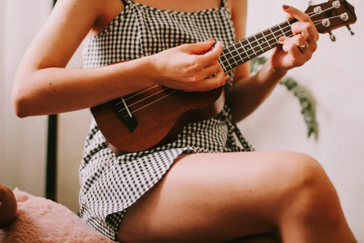 Dziewczyna w kratkę uczy się, jak nastroić ukulele sopranowe, ćwicząc akordy.