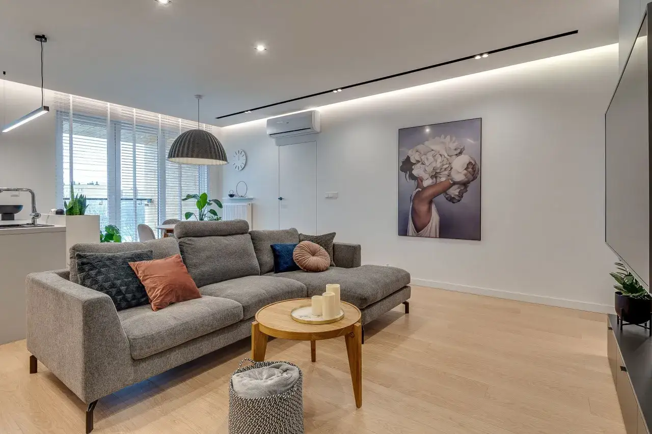 Nowoczesny salon w projekcie mieszkania 70m2. Szara kanapa, okrągły stolik kawowy, obraz z kobietą i kwiatami.