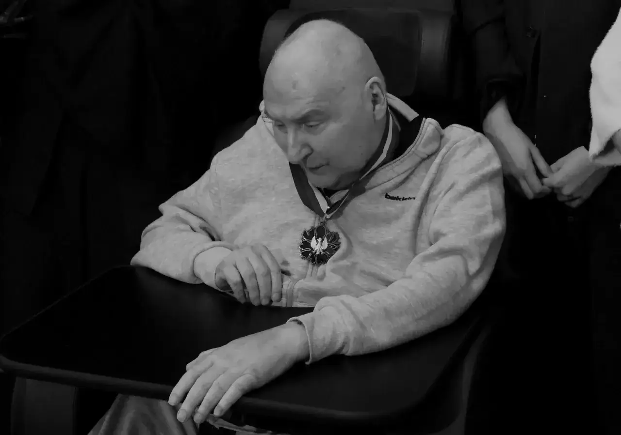 Wojciech Trzciński w okularach i z medalem na szyi, w tle osoby trzymające się za ręce. Prywatne chwile.