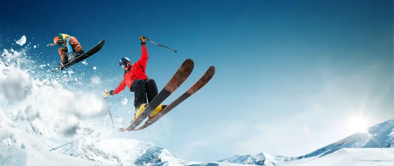 Narciarz i snowboardzista w powietrzu. Czy co jest bardziej kontuzyjne narty czy snowboard, zależy od umiejętności i stylu jazdy.