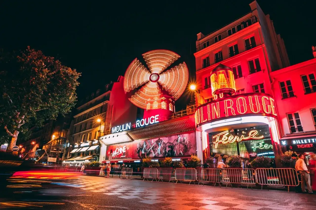 Nocny plac Pigalle w Paryżu, rozświetlony neonami Moulin Rouge i wirującym wiatrakiem.