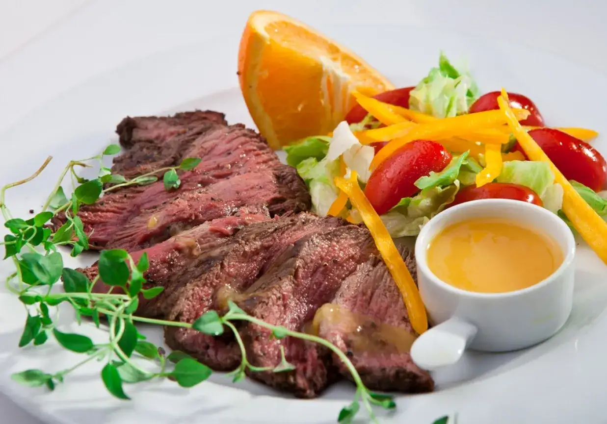 Pyszny stek z polędwicy wołowej, soczysty i idealnie wysmażony, podany z kolorową sałatką, ćwiartką pomarańczy i sosem.