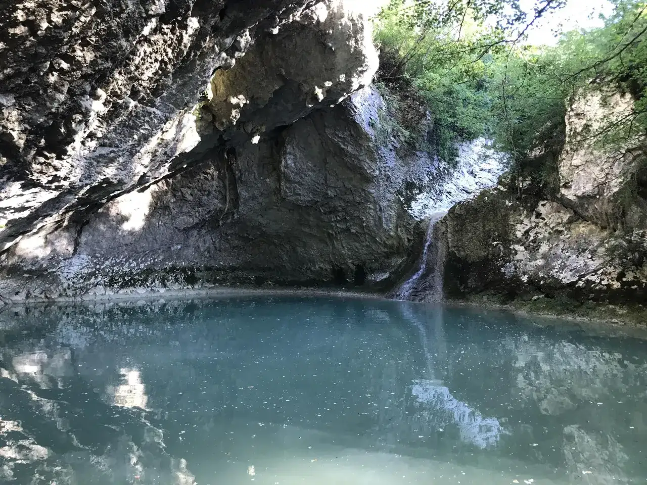 Ukryta zatoczka z turkusową wodą i niewielkimi wodospadami na Istrii. Skały porośnięte zielenią tworzą naturalną jaskinię.