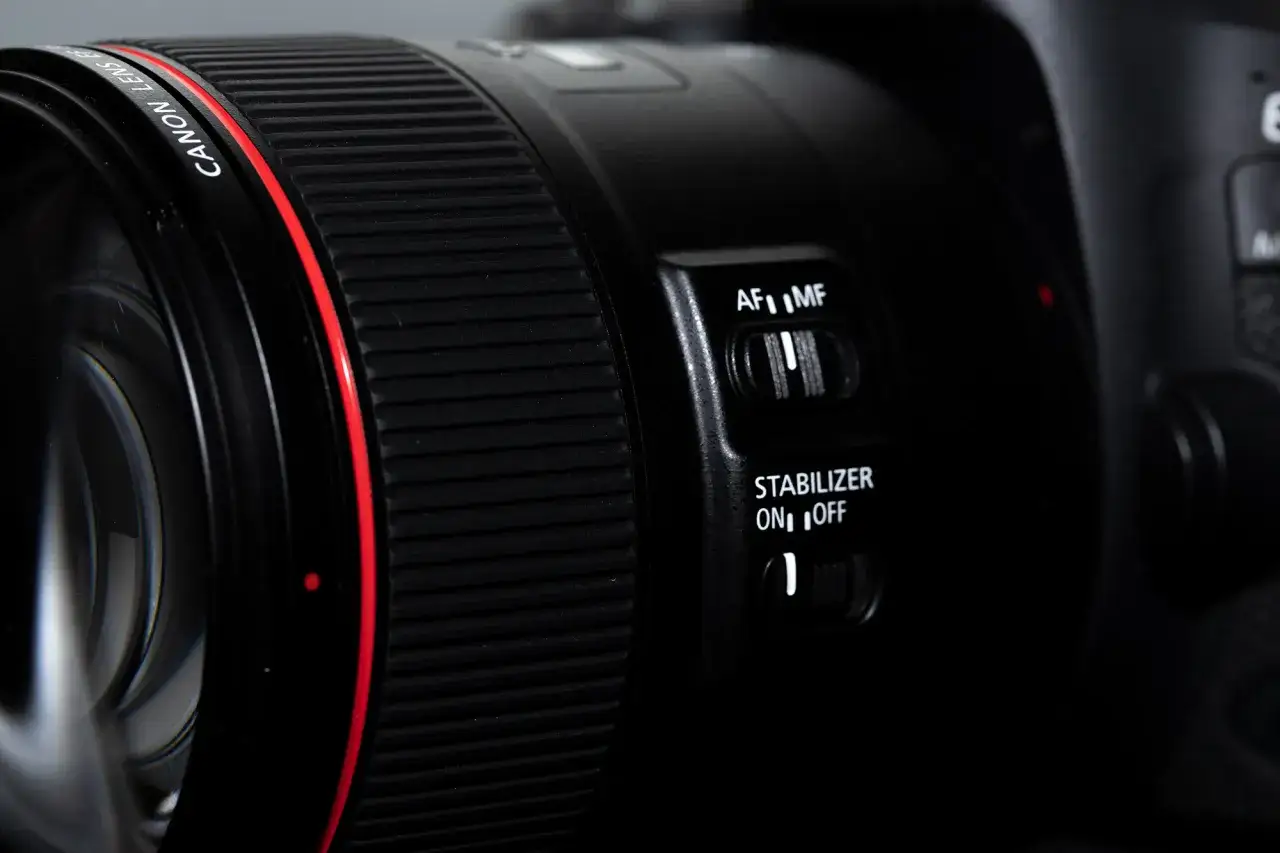 Zbliżenie na obiektyw Canon z włączoną stabilizacją obrazu w obiektywie. Widoczny przełącznik AF/MF i stabilizacji.