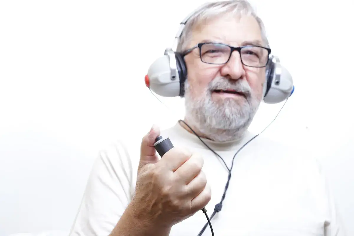 Starszy mężczyzna w okularach i słuchawkach przechodzi badanie słuchu. Lekarz audiolog zlecił mu test.