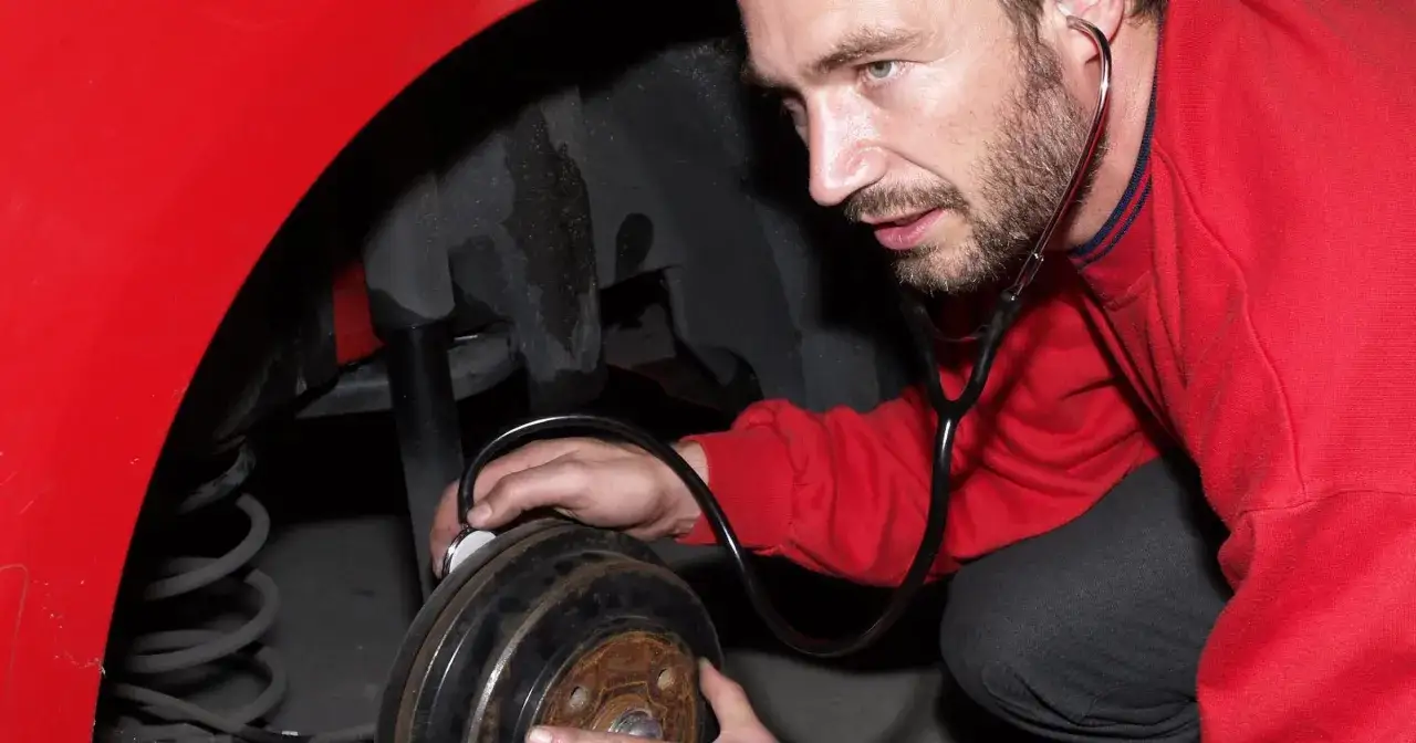 Mechanik nasłuchuje stukanie w kole za pomocą stetoskopu, próbując zdiagnozować problem.