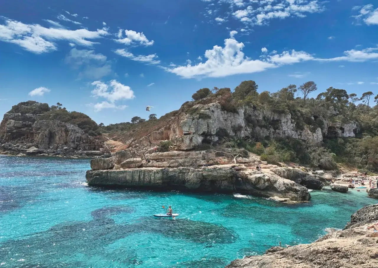 Turkusowe morze w Hiszpanii, skaliste wybrzeże, człowiek na desce SUP.