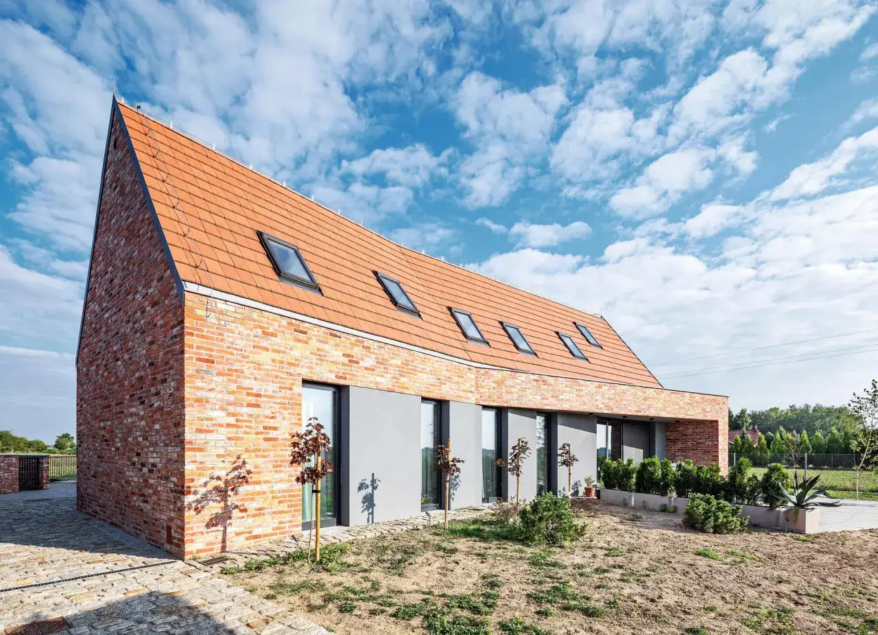 Nowoczesna elewacja budynku z cegły i tynku, z dachem pokrytym dachówką i oknami dachowymi.