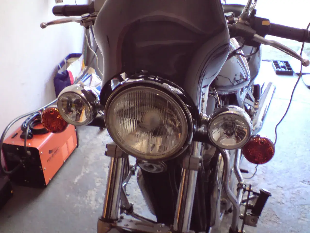 Motocykl z dodatkowymi światłami, okrągłymi, pomarańczowymi, zamontowanymi po bokach głównej lampy.