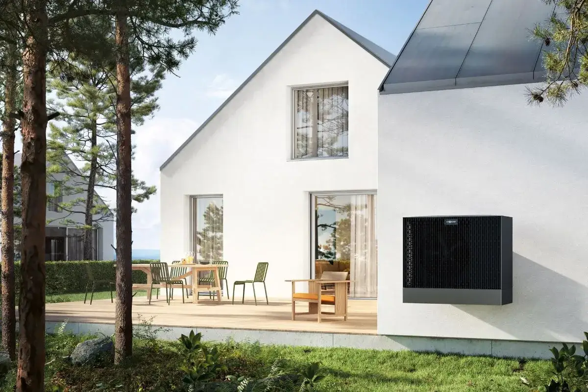 Nowoczesny dom z tarasem i meblami ogrodowymi. Na ścianie zamontowana jednostka grzewcza, idealna do uzyskania dofinansowania do ogrzewania elektrycznego.