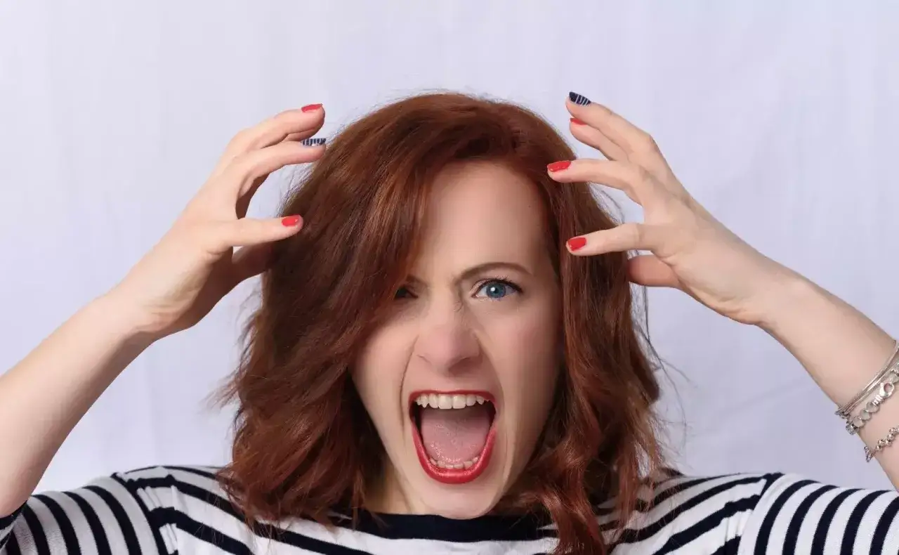 Kobieta z rudymi włosami krzyczy, trzymając się za głowę. Czy po botoksie boli głowa?