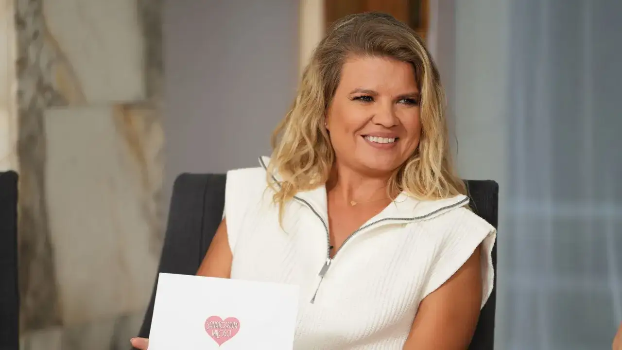 Uśmiechnięta kobieta z blond włosami trzyma kartkę z logo 