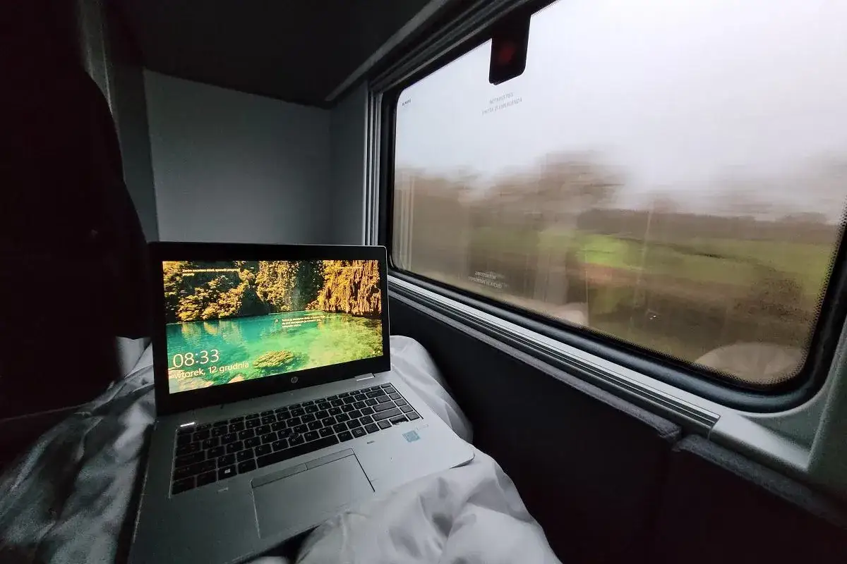 Laptop na tle krajobrazu za oknem pociągu. Podróż z Warszawy do Wiednia w komfortowych warunkach.