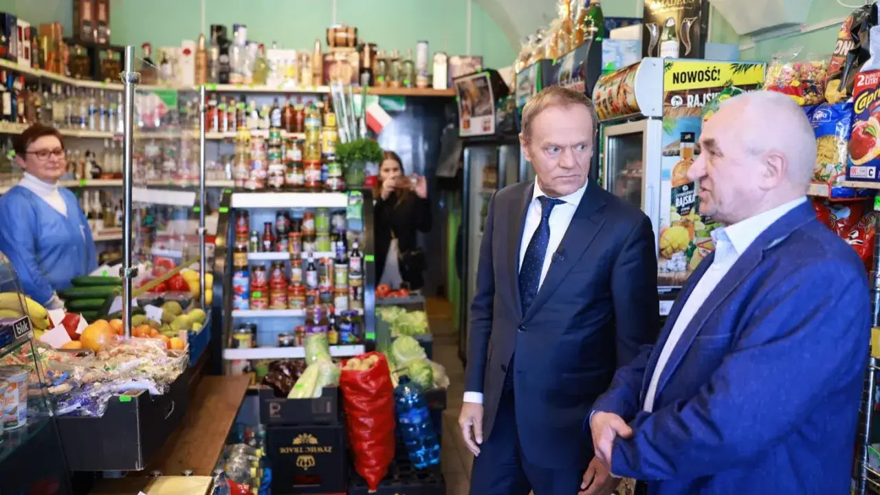 Donald Tusk w sklepie, rozmawia z mężczyzną. Czy Tusk to lewica czy prawica? W tle półki z produktami.