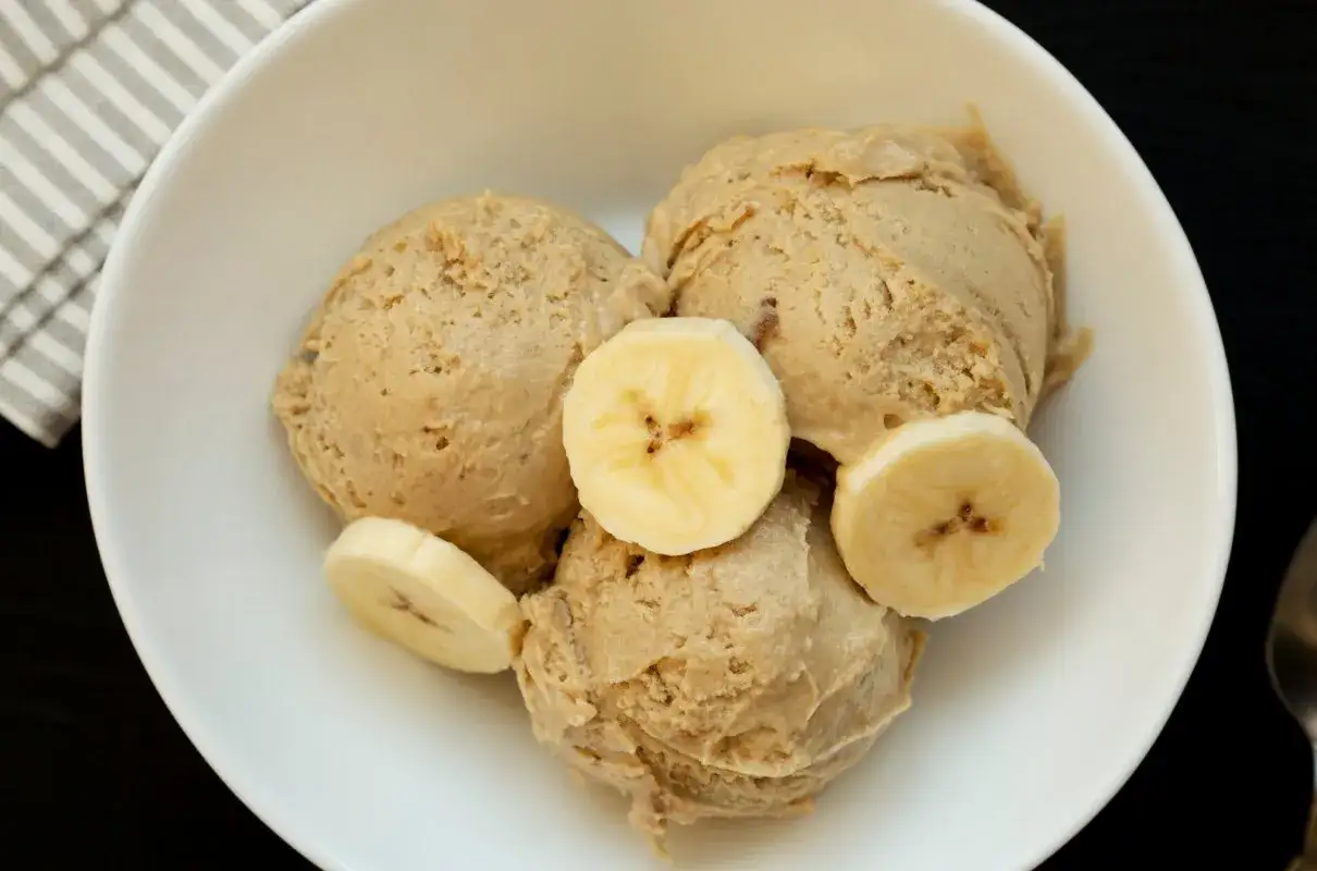 Trzy gałki kremowych lodów bananowych w białej misce, ozdobione plasterkami banana. Idealne na letnie orzeźwienie.