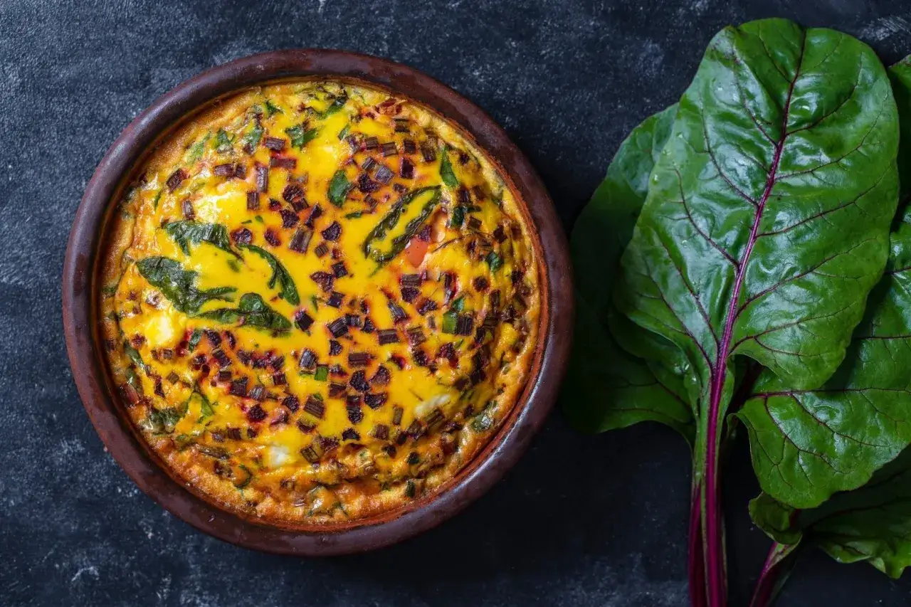 Pyszny farsz do tarty na słono z burakami i zielonymi liśćmi, w glinianej formie, obok świeże liście buraka.