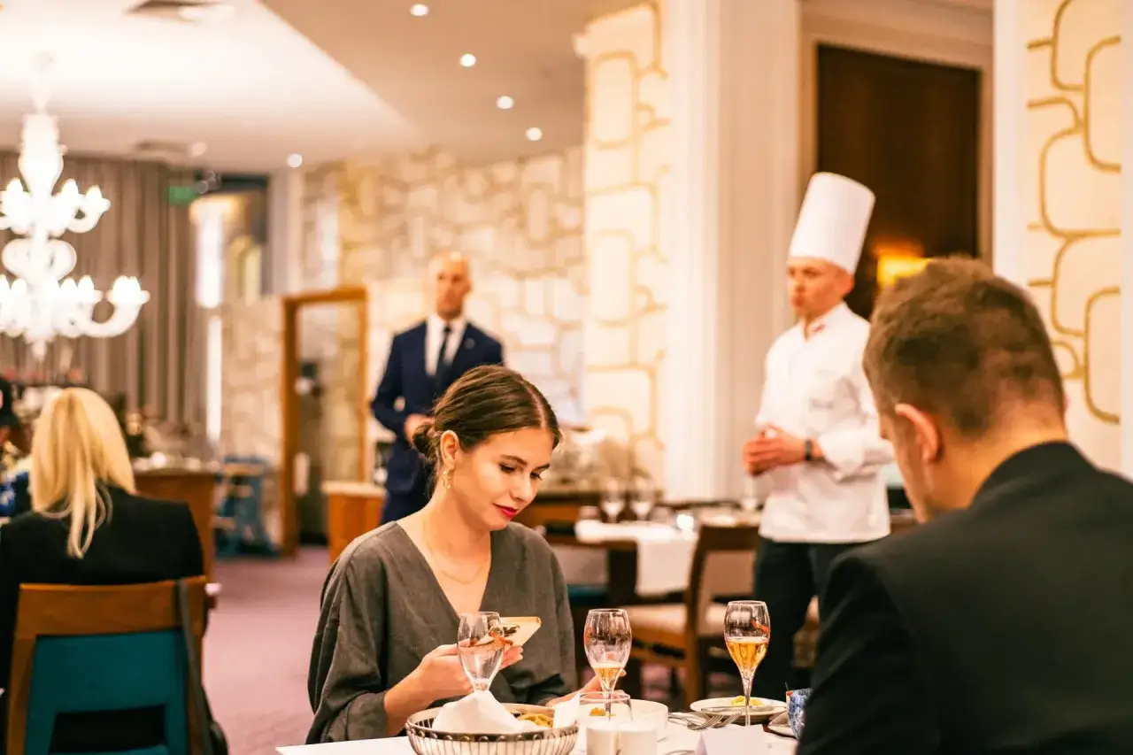 Pierwsza randka z Tindera w eleganckiej restauracji. Ona sprawdza telefon, on patrzy w bok. Szef kuchni prezentuje danie.