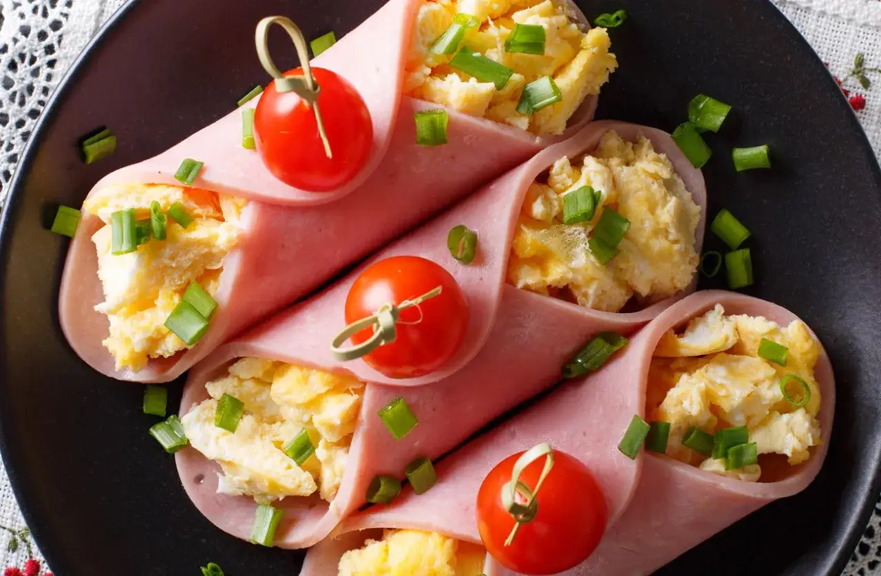 Roladki z szynki z jajecznicą i szczypiorkiem, ozdobione pomidorkami koktajlowymi. Pyszna przekąska na śniadanie.