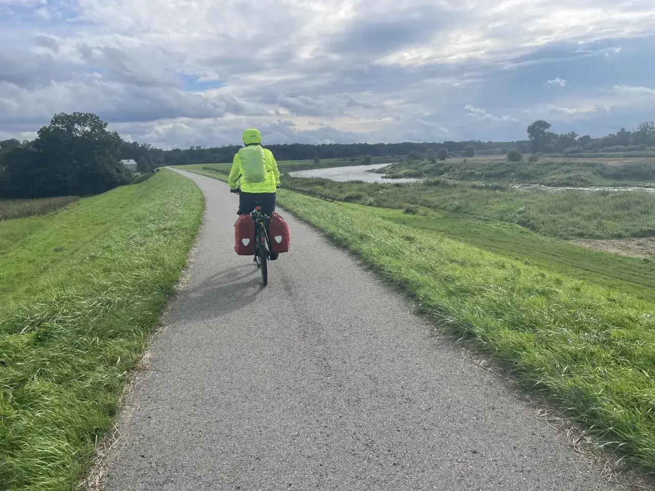 Rowerzysta w jaskrawej kurtce jedzie po niepołomickiej trasie rowerowej wzdłuż rzeki.